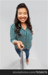technology and people concept - happy asian woman taking picture with selfie stick over grey background. happy asian woman taking picture with selfie stick