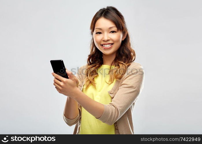 technology and people concept - happy asian woman using smartphone over grey background. happy asian woman using smartphone