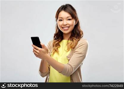 technology and people concept - happy asian woman using smartphone over grey background. happy asian woman using smartphone