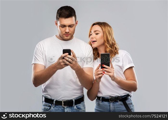 technology and people concept - happy couple in white t-shirts with smartphones over grey background. happy couple in white t-shirts with smartphones
