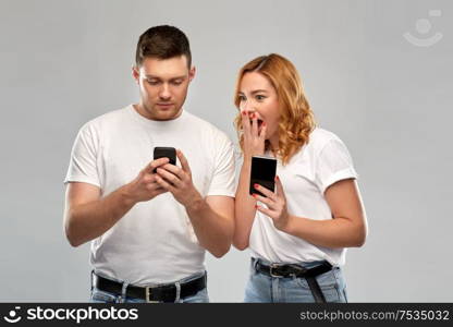 technology and people concept - happy couple in white t-shirts with smartphones over grey background. happy couple in white t-shirts with smartphones