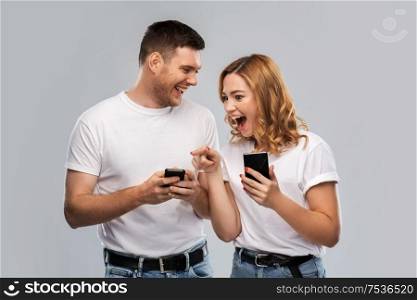 technology and people concept - happy couple in white t-shirts with smartphones over grey background. happy couple in white t-shirts with smartphones