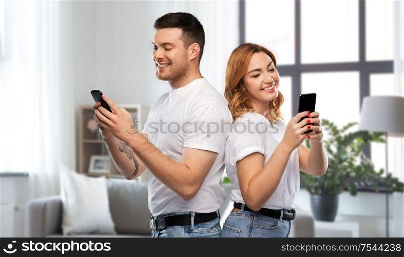technology and people concept - happy couple in white t-shirts with smartphones over home background. happy couple in white t-shirts with smartphones
