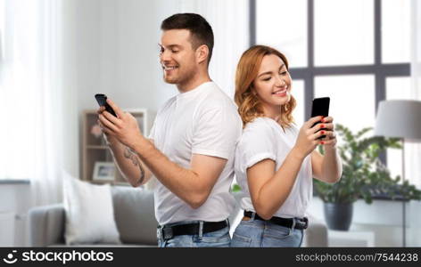 technology and people concept - happy couple in white t-shirts with smartphones over home background. happy couple in white t-shirts with smartphones