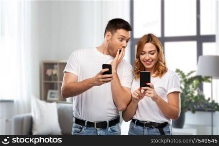 technology and people concept - happy couple in white t-shirts with smartphones over home background. happy couple in white t-shirts with smartphones
