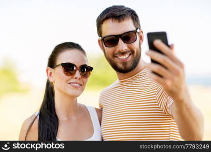 technology and people concept - happy couple taking selfie by smartphone in summer. happy couple taking selfie by smartphone in summer