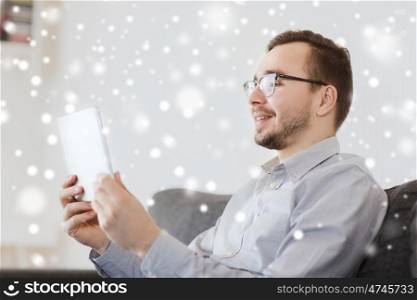 technology and people concept - happy man working with tablet pc computer at home over snow. smiling man working with tablet pc at home