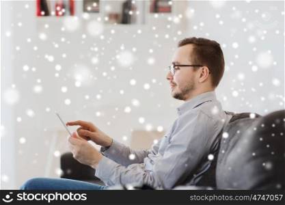 technology and people concept - happy man working with tablet pc computer at home over snow. smiling man working with tablet pc at home