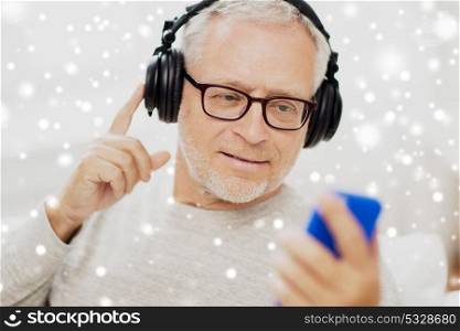 technology and people concept - happy senior man with smartphone and headphones listening to music and singing over snow. happy senior man with smartphone and headphones