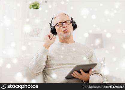 technology and people concept - happy senior man with tablet pc computer and headphones listening to music and singing at home over snow. senior man with tablet pc and headphones at home