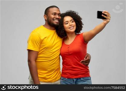 technology and people concept - happy smiling african american couple taking selfie by smartphone over grey background. african american couple takes selfie by smartphone
