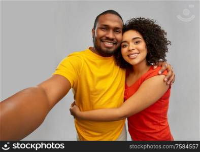 technology and people concept - happy smiling african american couple taking selfie over grey background. happy smiling african american couple takes selfie