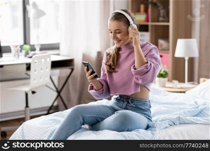 technology and people concept - happy smiling girl in headphones with smartphone at home. girl in headphones with smartphone at home