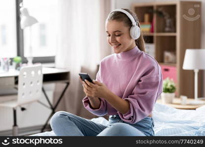 technology and people concept - happy smiling girl in headphones with smartphone at home. girl in headphones with smartphone at home