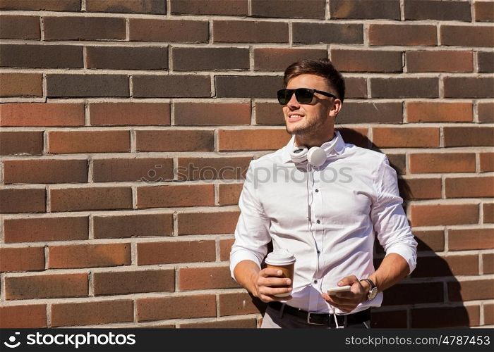 technology and people concept - happy smiling young man in sunglasses with smartphone and coffee cup on city street. man with smartphone and coffee cup on city street