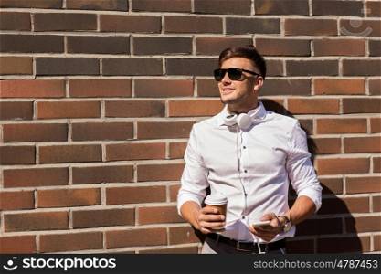 technology and people concept - happy smiling young man in sunglasses with smartphone and coffee cup on city street. man with smartphone and coffee cup on city street
