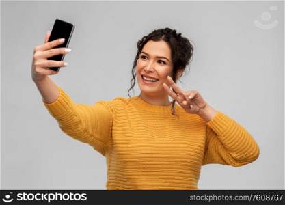 technology and people concept - happy smiling young woman taking selfie by smartphone over grey background. smiling young woman taking selfie by smartphone