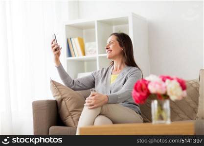 technology and people concept - happy woman taking selfie smartphone at home. happy woman taking selfie smartphone at home
