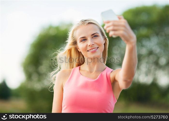 technology and people concept - happy young beautiful woman with smartphone taking selfie outdoors. happy woman taking selfie with smartphone outdoors