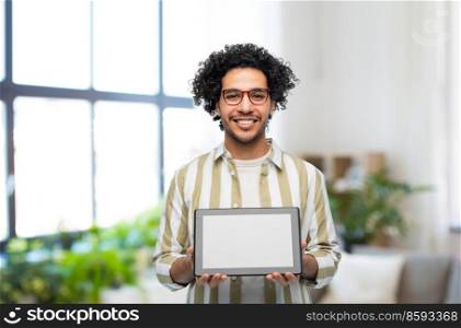 technology and people concept - happy young man in glasses with tablet pc computer over home room background. happy young man with tablet pc computer at home