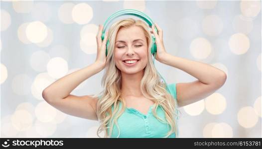 technology and people concept - happy young woman or teenage girl with headphones listening to music over holidays lights background. happy young woman or teenage girl with headphones