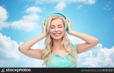 technology and people concept - happy young woman or teenage girl with headphones listening to music over blue sky and clouds background. happy young woman or teenage girl with headphones