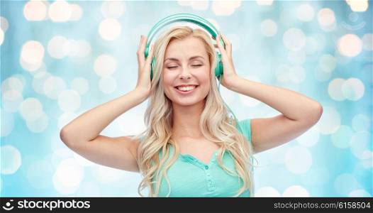 technology and people concept - happy young woman or teenage girl with headphones listening to music over blue holidays lights background. happy young woman or teenage girl with headphones