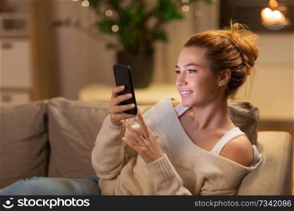technology and people concept - happy young woman with smartphone at home in evening. happy young woman with smartphone at home