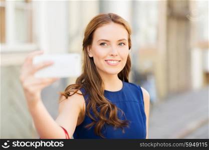 technology and people concept - happy young woman with smartphone taking selfie on city street. happy woman taking selfie with smartphone in city