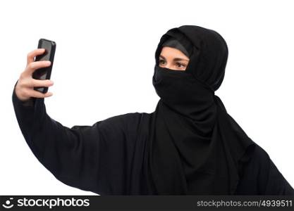 technology and people concept - muslim woman in hijab taking selfie with smartphone over white background. muslim woman in hijab taking selfie by smartphone