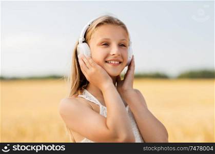 technology and people concept - portrait of happy girl in headphones on cereal field listening to music in summer. happy girl in headphones on cereal field in summer