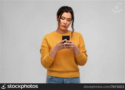 technology and people concept - sad woman using smartphone over grey background. sad woman using smartphone