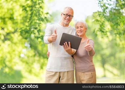 technology and people concept - senior couple with tablet pc computer showing thumbs up over green natural background. senior couple with tablet pc showing thumbs up