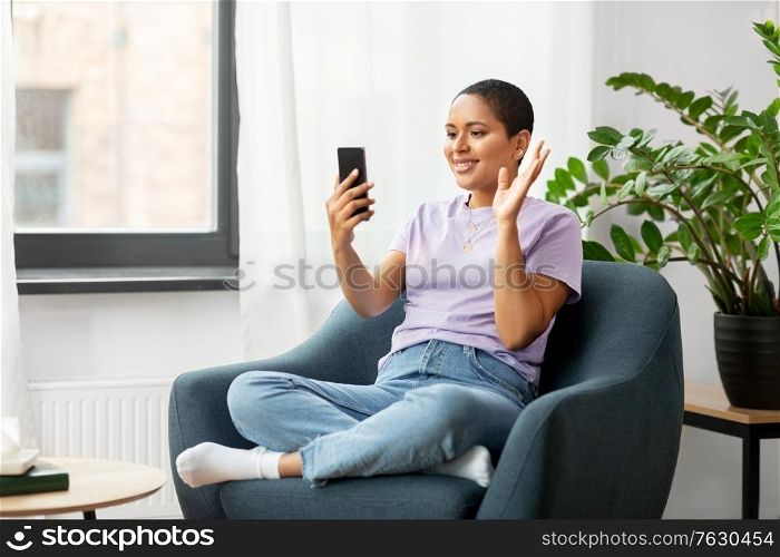 technology and people concept - smiling african american woman in glasses with smartphone having video call at home. woman with smartphone having video call at home