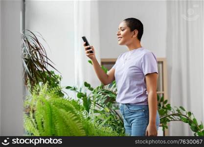 technology and people concept - smiling african american woman with smartphone and indoor plants at home. african american woman with smartphone at home