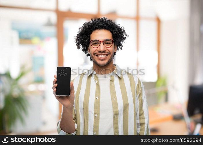 technology and people concept - smiling man in glasses showing smartphone with blank screen over office background. happy man in glasses showing smartphone at office