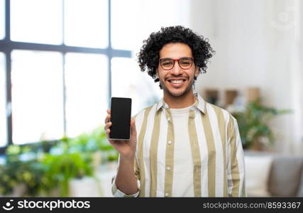 technology and people concept - smiling man in glasses showing smartphone with blank screen over home room background. smiling man in glasses showing smartphone at home