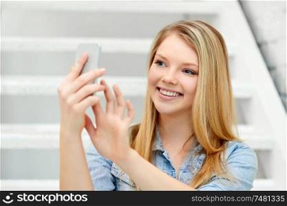 technology and people concept - smiling teenage girl taking selfie by smartphone on stairs. teenage girl taking selfie by smartphone on stairs