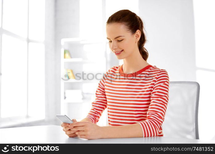 technology and people concept - smiling teenage girl with smartphone sitting at table. teenage girl with smartphone sitting at table