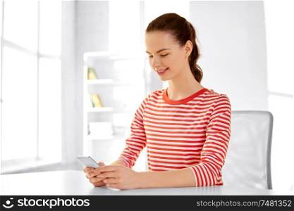 technology and people concept - smiling teenage girl with smartphone sitting at table. teenage girl with smartphone sitting at table