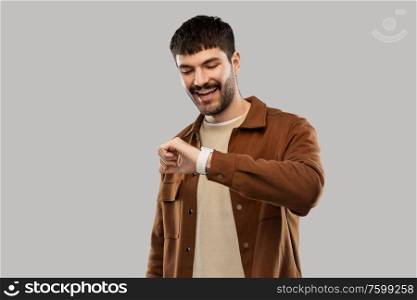 technology and people concept - smiling young man with smart watch over grey background. smiling young man with smart watch