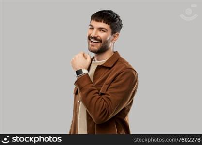 technology and people concept - smiling young man with smart watch over grey background. smiling young man with smart watch