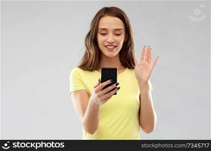 technology and people concept - smiling young woman or teenage girl in blank yellow t-shirt having video call smartphone and waving hand over grey background. smiling teenage girl having video call smartphone