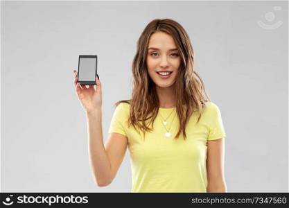 technology and people concept - smiling young woman or teenage girl in yellow t-shirt holding smartphone with blank screen over grey background. young woman or teenage girl holding smartphone