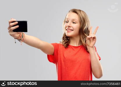 technology and people concept - smiling young woman or teenage girl in blank red t-shirt taking selfie by smartphone over grey background. smiling teenage girl taking selfie by smartphone