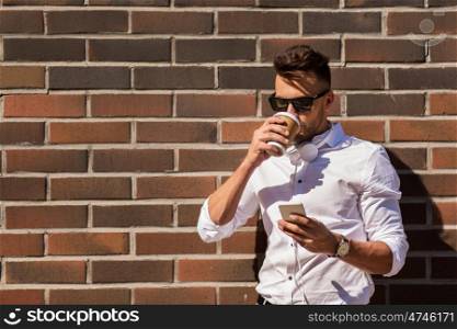 technology and people concept - young man in sunglasses with smartphone drinking coffee on city street. man with smartphone and coffee cup on city street