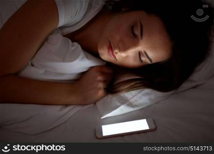 technology and people concept - young woman with smartphone sleeping in bed at home at night. woman with smartphone sleeping in bed at night