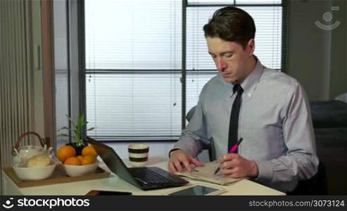 Technology and white people working at home with pc, young business man at work with laptop computer and newspaper while having breakfast in living room, businessman drinking coffee, busy male manager