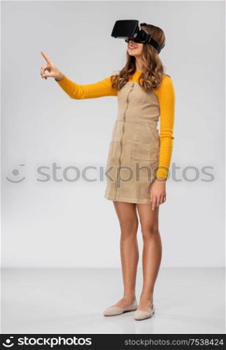technology, augmented reality and entertainment concept - happy teenage girl with virtual headset or vr glasses over grey background. teenage girl in vr glasses over grey background