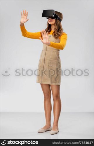 technology, augmented reality and entertainment concept - happy teenage girl with virtual headset or vr glasses over grey background. teenage girl in vr glasses over grey background